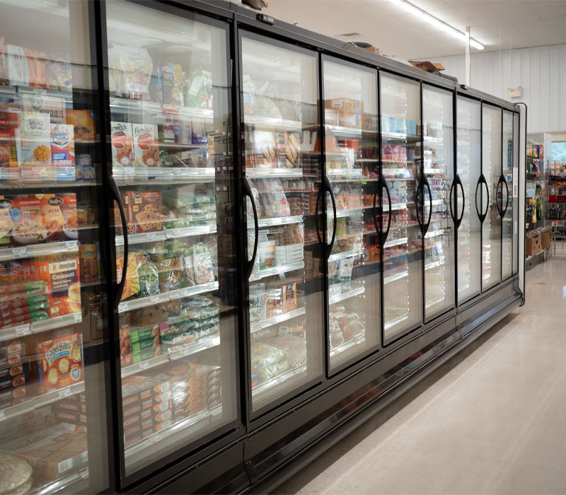 A row of glass-door reach-in freezers in a grocery store, filled with packaged goods