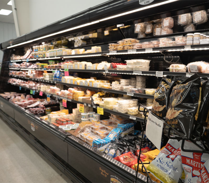 Long grocery store display case with deli salads, cheese wedges, and deli meat.
